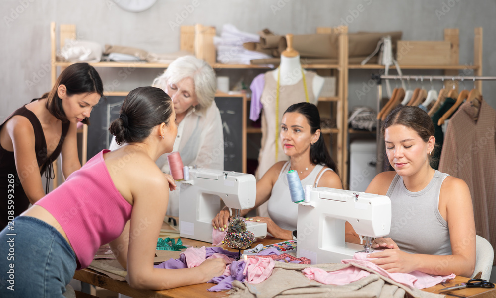 Obraz premium Older and younger women spending time together sewing in cozy workroom, friendly chatting while using machines and drawing paper templates during hands-on leisure time..