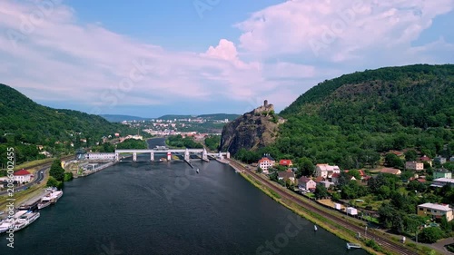 Aerial view of Strekov Castle overlooking the Elbe River, with lush green hills, residential buildings, and a bridge connecting both riverbanks in the Czech Republic