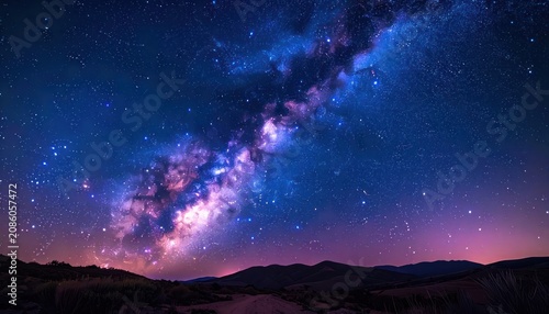 A breathtaking view of the Milky Way galaxy stretches across the night sky above silhouetted hills, dotted with countless stars and vibrant nebulae in hues of blue and purple.