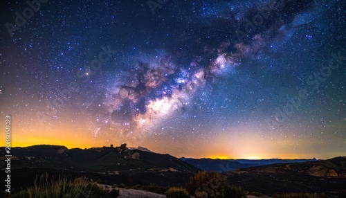 The Milky Way galaxy arches majestically across a starry night sky above a silhouetted mountain range.