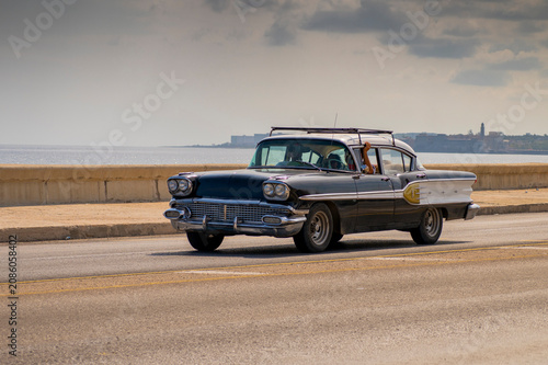Classic black American vintage car driving along Havana Malecón in Cuba