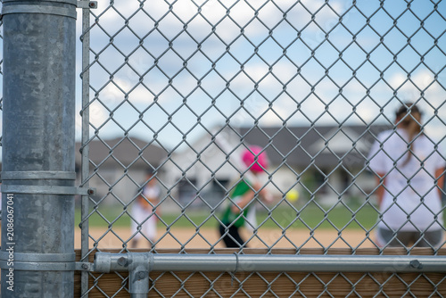 Selective focus on a fence during a softball game with blurred players in action under a clear sky