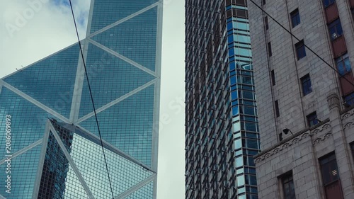 A towering modern skyscraper in Hong Kong, its geometric lattice facade reflecting light against a pale sky