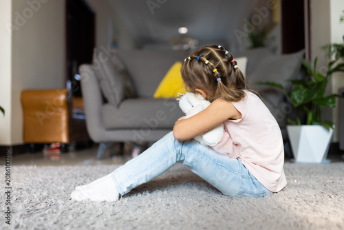 Tableau sur toile Young girl hugging stuffed toy while sitting on floor in living room