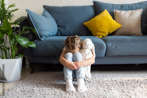 Obraz na plátně Sad young girl sitting on the floor and hugging a stuffed bunny at home