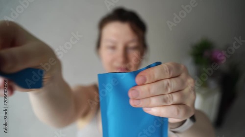 Static Shot Of Woman Tearing Open Blue Sachet And Removing Contents In Indoor Home Setting With Soft Natural Light And Blurred Background.