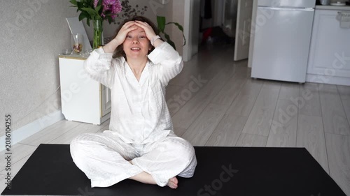 Static Shot Of Woman Sitting On Yoga Mat Performing Facial Massage And Playful Expressions In Bright Home Living Room.