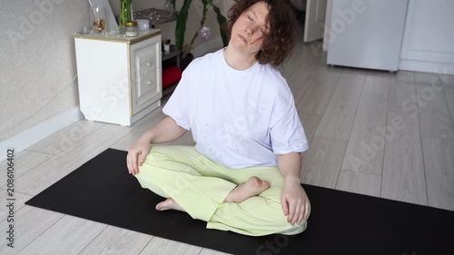 Static Shot Of Woman Meditating On Yoga Mat And Lowering Hands In Bright Home Interior With Hardwood Floor And Minimal Decor.