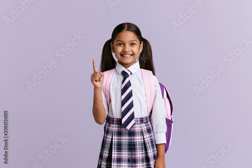 Schoolgirl student smiling and pointing up wearing a uniform with a backpack child
