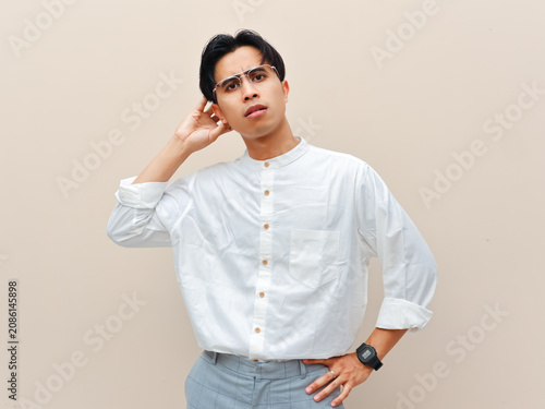 Cuadro en lienzo Confused young Asian man scratching his head and looking puzzled against plain background