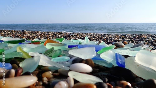 Colored sea glass with beach pebbles and shells in the mediterranean coast and in the background sea and waves with sunset and sky, sandy beach with coast glass, beach glass.