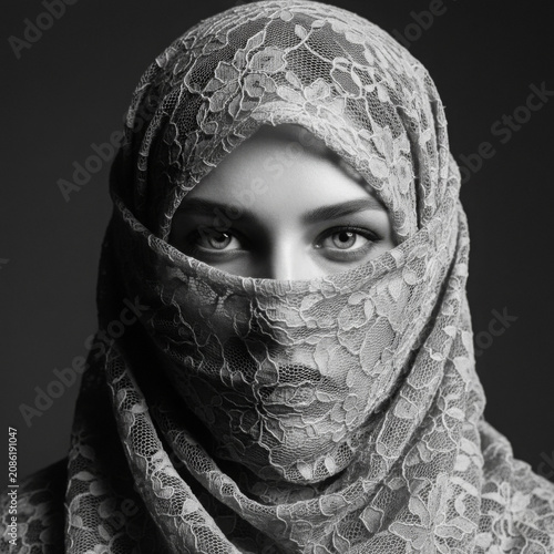 Lace veil covering a woman face showing intense beautiful eyes in a dramatic black and white fine art studio portrait