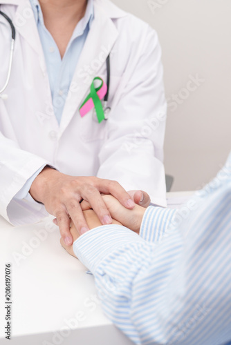 doctor hold patient hand to comfort and support with empathy. green and pink ribbon to patient for concept of October Metastatic Breast Cancer Awareness month, National Cancer Survivors Month
