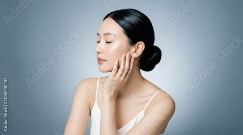 Portrait of a young asian woman with glowing skin touching her face