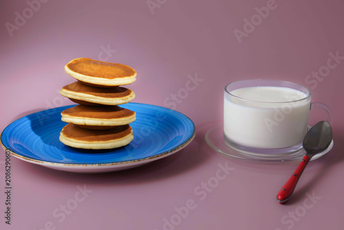 Stack of fluffy golden pancakes on a blue plate, served with a clear glass of milk and a spoon, ready for breakfast