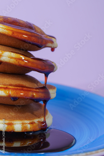 Pancakes stack with golden syrup dripping down onto a bright blue plate, offering a sweet breakfast or brunch meal