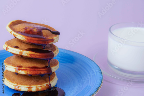 Stacked pancakes drizzled with syrup on a blue plate, serving a sweet breakfast beside a glass of fresh milk