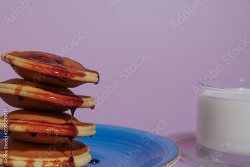 Stack of fluffy pancakes topped with golden syrup dripping down, served on a blue plate with a glass of milk