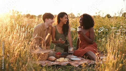 friends laughing at outdoor picnic with wine cheese and berries in golden hour field