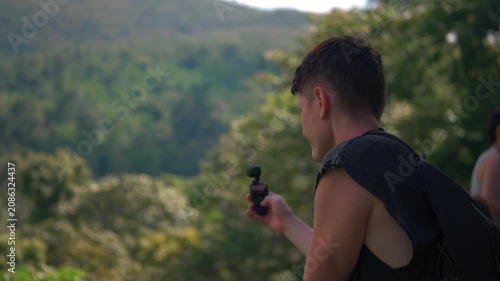 Male traveler filming tropical rainforest mountains with pocket camera during jungle adventure, Travel creator capturing lush forest scenery, mountain wilderness and tropical nature 4k