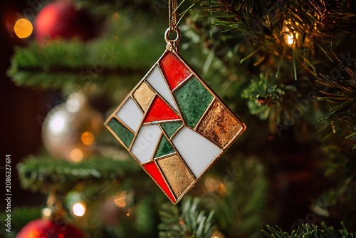 Festive stained glass Christmas ornament hanging on a tree with bokeh lights, creating a cozy holiday atmosphere.