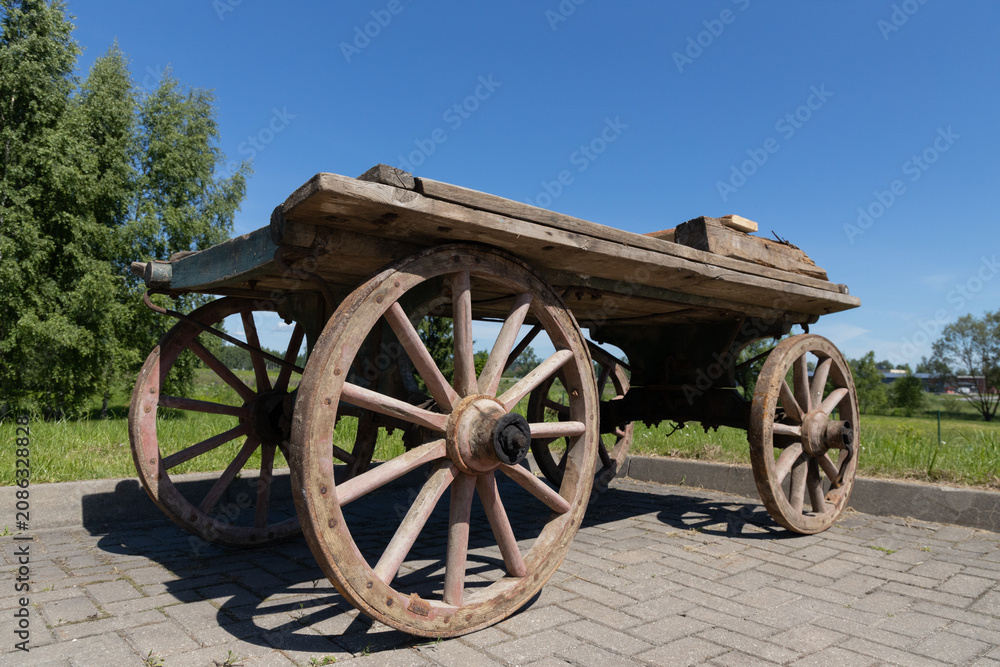 Obraz premium Rustic Wooden Cart With Large Spoked Wheels Parked On Paved Path In Sunny Countryside