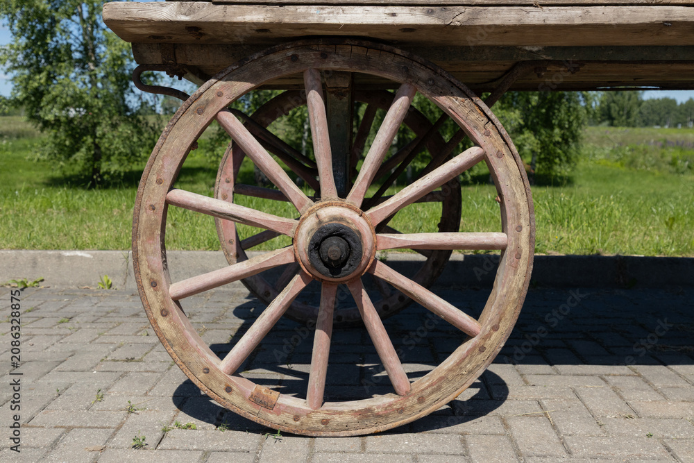 Obraz premium Rustic Wooden Wagon Wheel On Old Cart In Countryside Summer Landscape