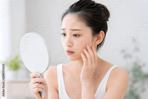 肌トラブルを鏡で確認する若い日本人女性
