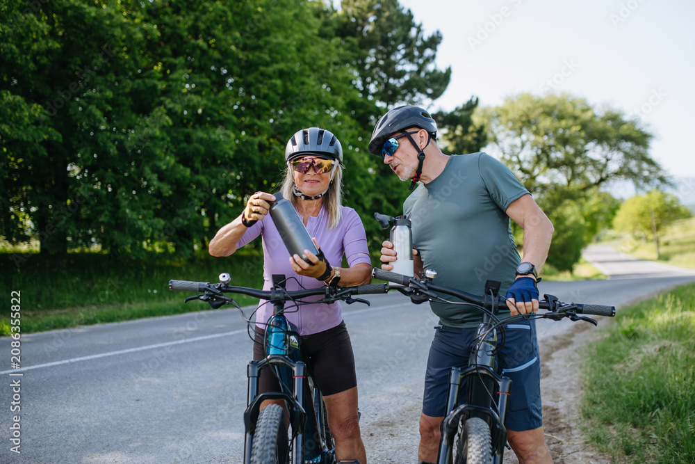 Obraz premium Mature couple resting and drinking water on electric bike tour.