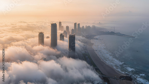 Aerial view of skyscrapers emerging from fog over a coastline at sunrise