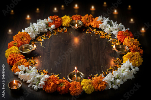 Diwali rangoli floral arrangement with marigolds and jasmine, traditional oil lamps on dark wood, festive Indian holiday background with copy space