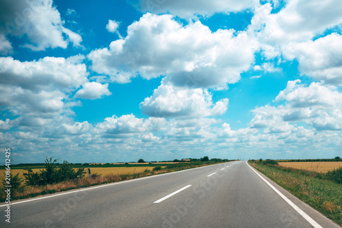 Open country road under blue sky with puffy clouds stretching to the distant horizon