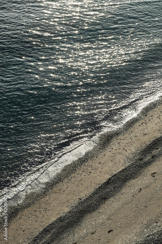Sparkling sun glint on waves washing over a sandy beach