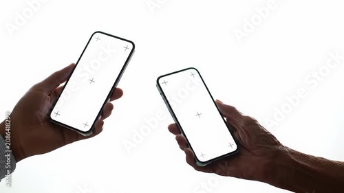 Diverse hands with various skin tones interact with sleek modern smartphones featuring blank white screens in a shadowless white studio. Concept of modern digital progress and connectivity