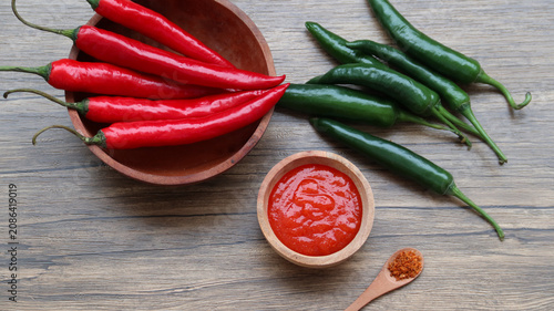 Foto Chilli sauce and fresh peppers on wooden background