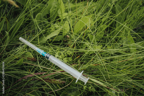 Photos A used syringe lying in long, green grass illustrates the pollution of medical waste, public health risks, and improper disposal in the natural environment