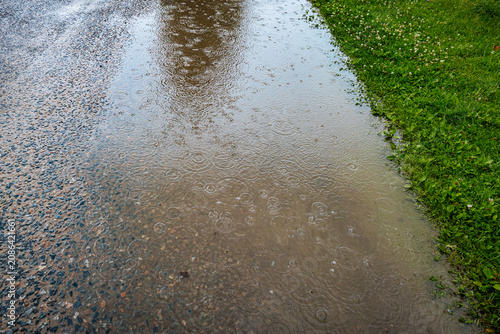 Foto Flooded gravel road covered with rainwater, circular raindrop ripples, reflections, and green grass along the edge