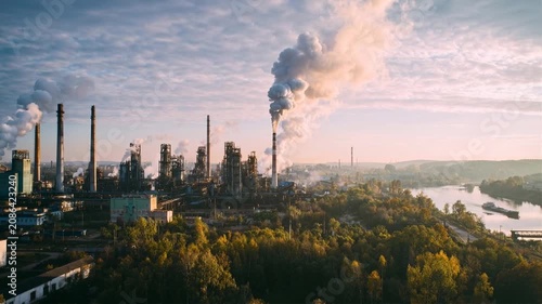Industrial factory complex emitting smoke against a cloudy sky at sunrise