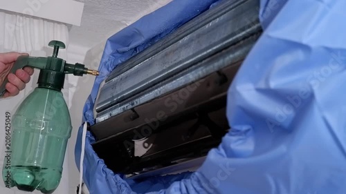 Professional worker cleaning and servicing an indoor air conditioner unit with a special tool