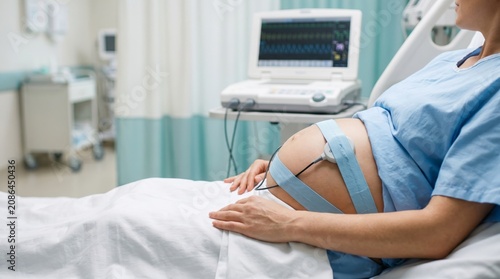 A pregnant woman lying on a hospital bed with a fetal monitor attached. Concept maternity, healthcare, pregnancy, medical technology, prenatal care, hospital setting. Generative AI