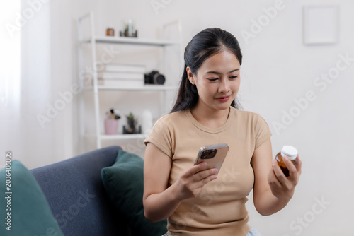 Fotografie Calm young asian woman sitting on living room sofa holding smartphone and checki
