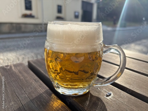 A small glass of beer on a table in a garden pub in the reflection of the summer sun