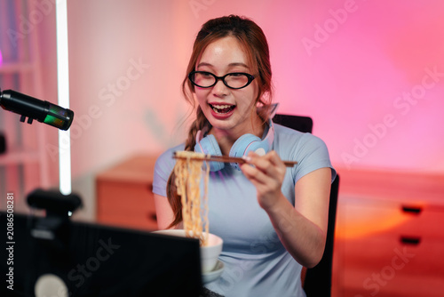 Young woman streamer eats noodles live broadcast from neon home