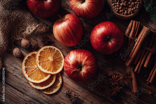 Autumn harvest of fresh red apples, dried orange slices, cinnamon sticks, and spices on a rustic wooden table.