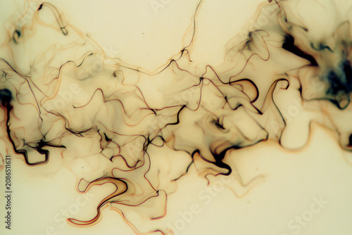 Abstract swirling smoke or ink patterns in a light colored liquid, creating organic shapes and textures.