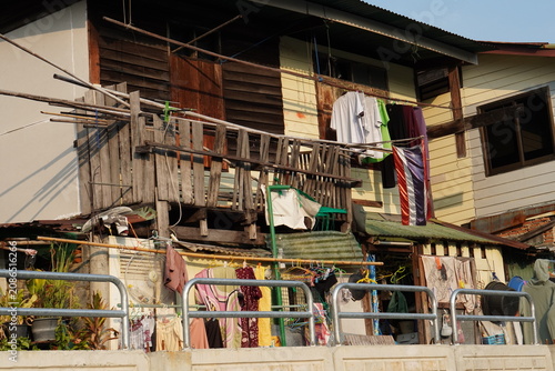 Tableau sur toile Aged wooden residential building in Thailand featuring a Thai flag, hanging laundry, and various everyday household items on a makeshift balcony