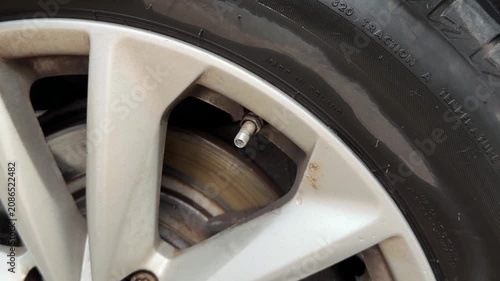 Close up of hand unscrewing black plastic valve stem cap from a car wheel tire.