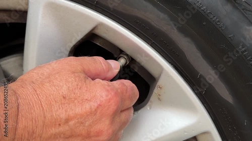 Close up of man hands connecting air compressor pump hose nozzle to car tire valve.