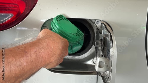 Close up of green fuel pump nozzle inserted into a white car gas tank during refueling.