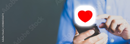 Man holding smartphone with red heart icon, online dating and social media engagement concept